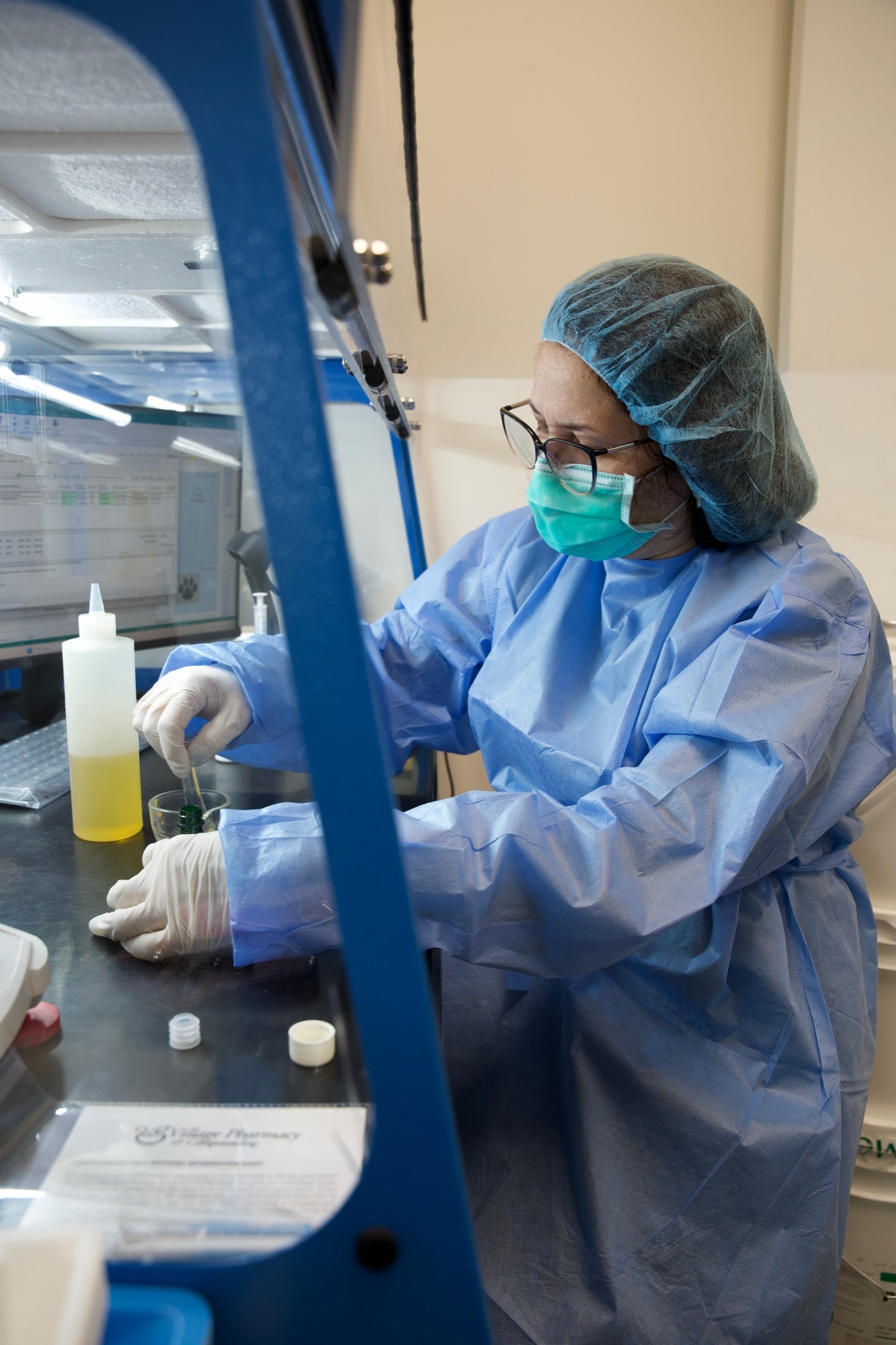 A Village pharmacist in sterile gear mixing a compounded preparation under the lab hood